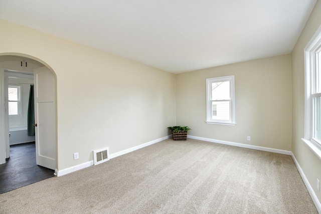 carpeted spare room with arched walkways, visible vents, and baseboards