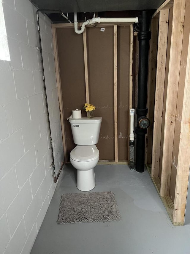 bathroom featuring concrete flooring, toilet, and concrete block wall