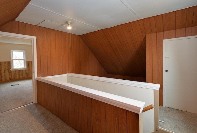 interior space featuring visible vents, lofted ceiling, carpet, an upstairs landing, and wood walls