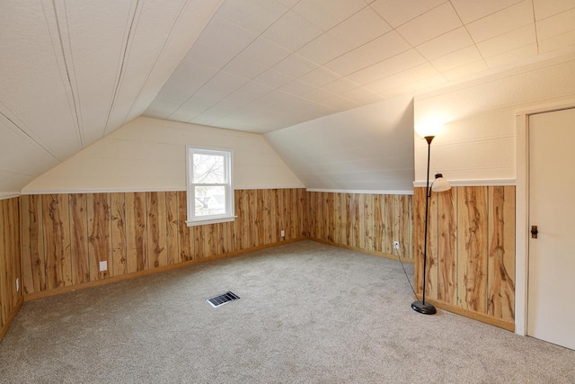 additional living space featuring wood walls, visible vents, vaulted ceiling, and carpet flooring