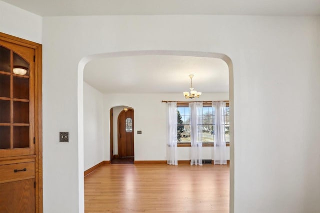 foyer entrance with visible vents, baseboards, arched walkways, light wood-style floors, and a chandelier