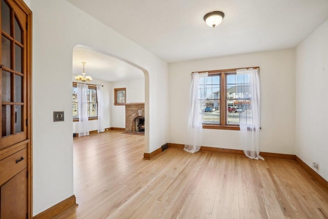 empty room featuring arched walkways, a fireplace, light wood-type flooring, and baseboards