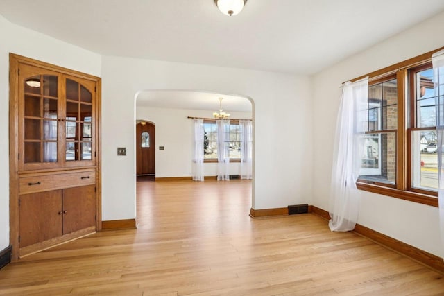 unfurnished dining area with arched walkways, visible vents, light wood finished floors, and baseboards