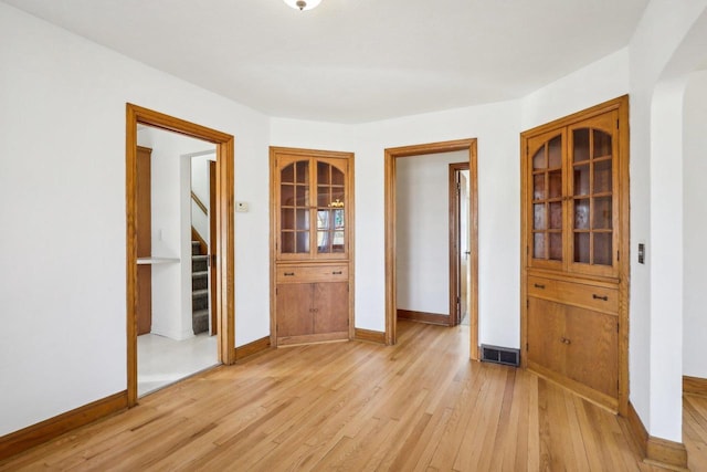 unfurnished room with light wood-type flooring, baseboards, visible vents, and stairway