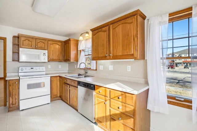 kitchen with brown cabinets, a sink, white appliances, light countertops, and light floors