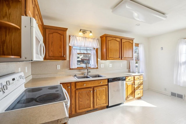 kitchen with visible vents, brown cabinets, a sink, white appliances, and light countertops