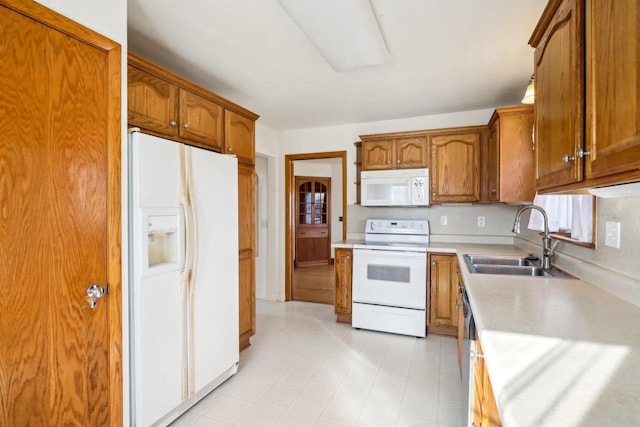 kitchen featuring light floors, light countertops, brown cabinets, white appliances, and a sink