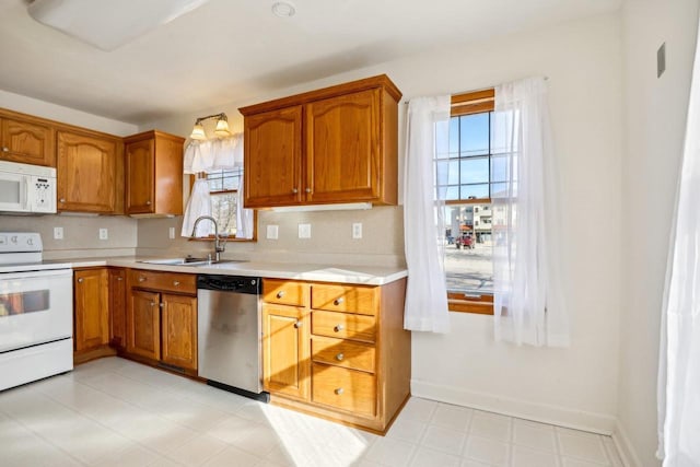 kitchen featuring brown cabinets, a sink, white appliances, light countertops, and light floors