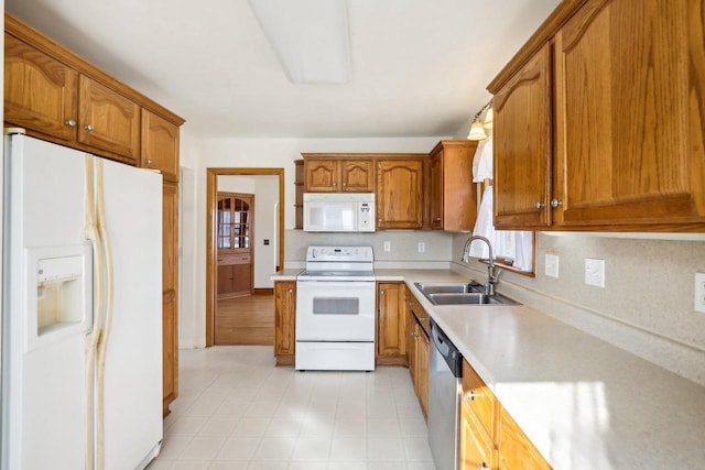 kitchen with white appliances, brown cabinetry, a sink, decorative backsplash, and light countertops