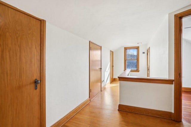 corridor with light wood-type flooring, baseboards, and vaulted ceiling