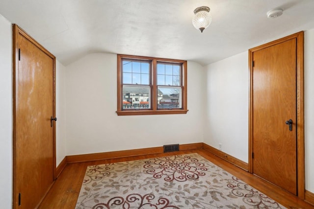 unfurnished bedroom with visible vents, lofted ceiling, baseboards, and wood finished floors