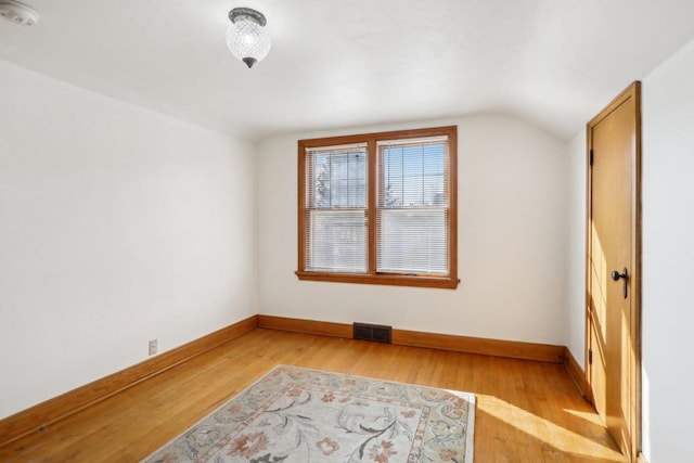 additional living space with light wood-type flooring, visible vents, baseboards, and vaulted ceiling