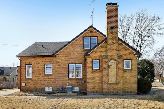 rear view of house with a shingled roof, brick siding, central AC, and a chimney