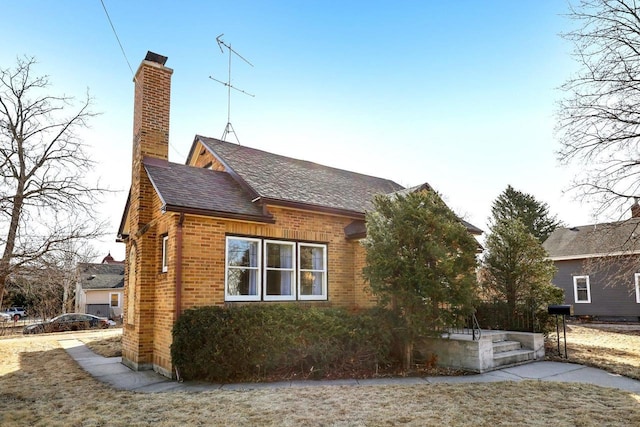 view of side of home featuring a shingled roof, brick siding, and a chimney