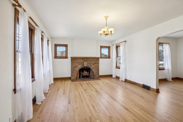 unfurnished living room with light wood-style flooring, a healthy amount of sunlight, arched walkways, and baseboards