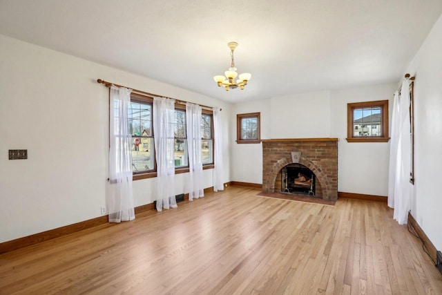 unfurnished living room with a wealth of natural light, a brick fireplace, baseboards, and light wood-style floors