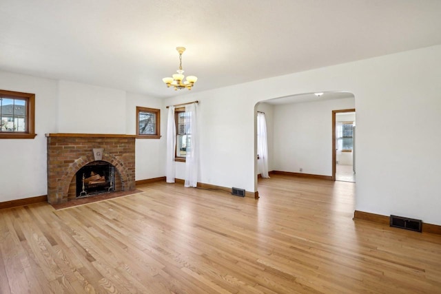 unfurnished living room with plenty of natural light, visible vents, arched walkways, and light wood-type flooring