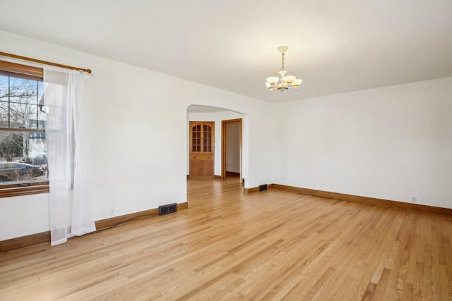 spare room featuring visible vents, light wood-style flooring, arched walkways, an inviting chandelier, and baseboards