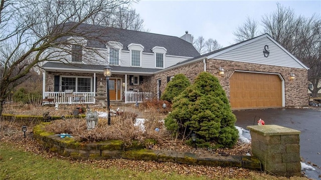 view of front of house with a garage, a chimney, aphalt driveway, covered porch, and brick siding