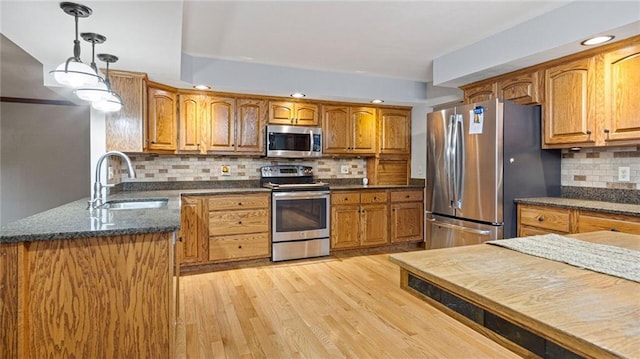 kitchen featuring light wood finished floors, appliances with stainless steel finishes, brown cabinets, decorative light fixtures, and a sink