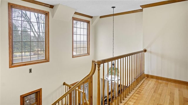 corridor featuring light wood finished floors, baseboards, ornamental molding, and an upstairs landing