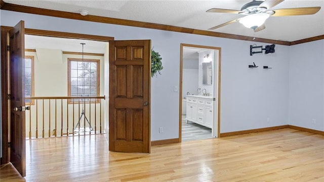 spare room featuring ornamental molding, a sink, light wood-style flooring, and baseboards