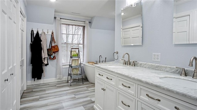 full bathroom with wood finished floors, double vanity, a freestanding tub, and a sink