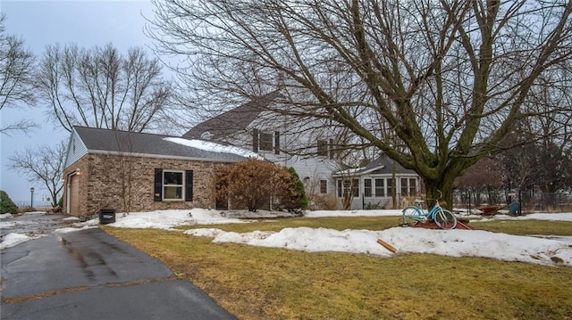 view of front of home featuring brick siding, a lawn, fence, a garage, and driveway