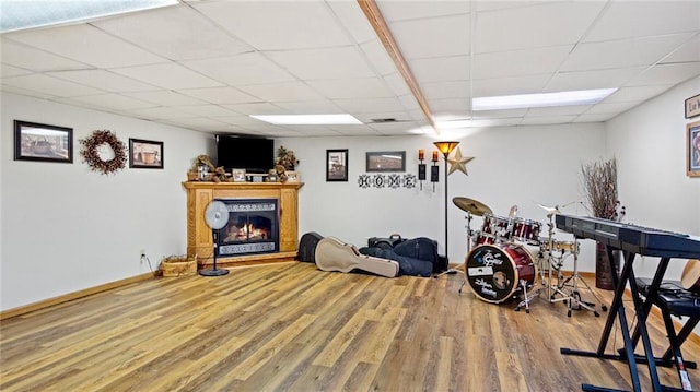 exercise area with a glass covered fireplace, a drop ceiling, wood finished floors, and baseboards