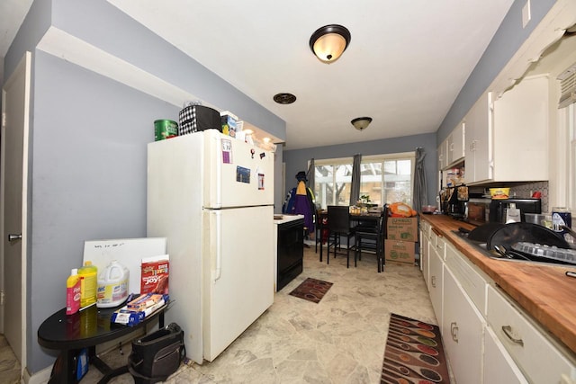 kitchen featuring wood counters, freestanding refrigerator, and white cabinetry