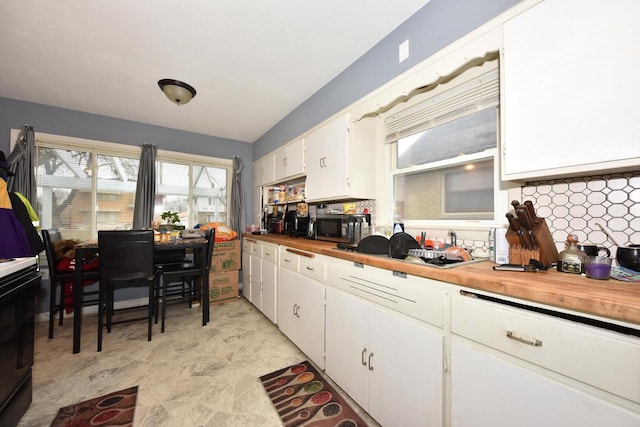 kitchen with black microwave, tasteful backsplash, white cabinetry, and wooden counters