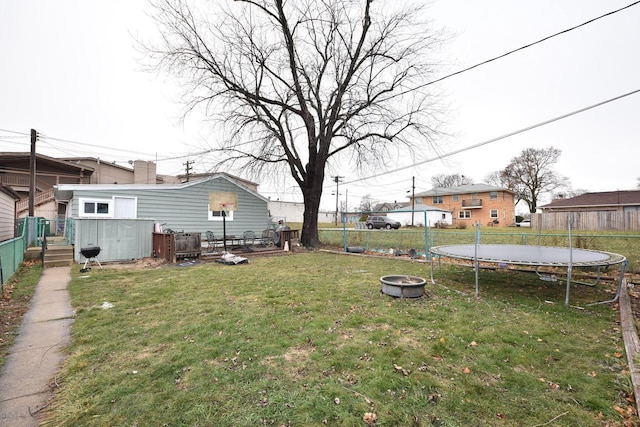 view of yard with a trampoline, an outbuilding, a shed, a fenced backyard, and a fire pit