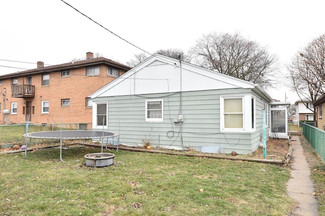 back of house with a trampoline, fence, and a lawn