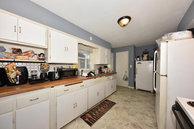 kitchen with white cabinets, decorative backsplash, butcher block countertops, freestanding refrigerator, and black microwave