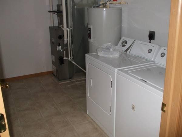 clothes washing area featuring laundry area, washing machine and dryer, water heater, and baseboards