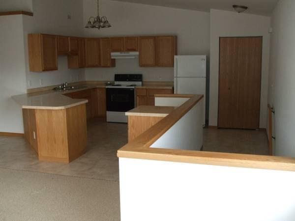 kitchen featuring electric stove, lofted ceiling, freestanding refrigerator, under cabinet range hood, and a notable chandelier