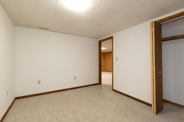 unfurnished bedroom featuring carpet floors, a closet, a paneled ceiling, and baseboards