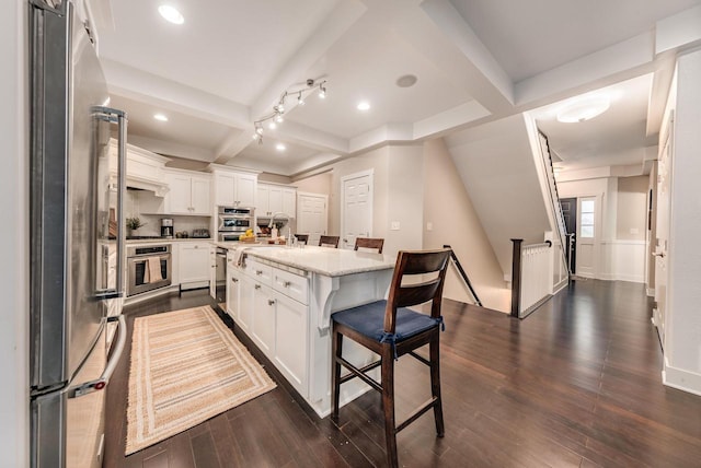 kitchen with stainless steel appliances, beam ceiling, white cabinets, and a kitchen breakfast bar