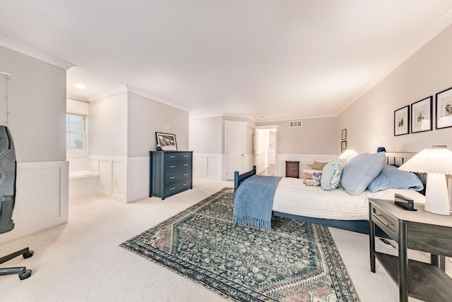 bedroom with visible vents, light colored carpet, a wainscoted wall, ensuite bath, and crown molding