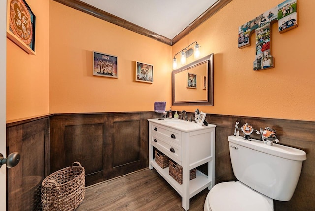 half bath with ornamental molding, wainscoting, wood finished floors, and toilet