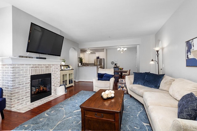 living area featuring ceiling fan with notable chandelier, arched walkways, a fireplace, and wood finished floors