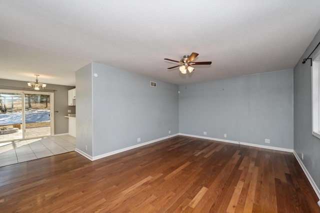 empty room with ceiling fan with notable chandelier, visible vents, baseboards, and wood finished floors