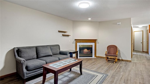 living room with light wood-type flooring, a glass covered fireplace, a textured ceiling, and baseboards