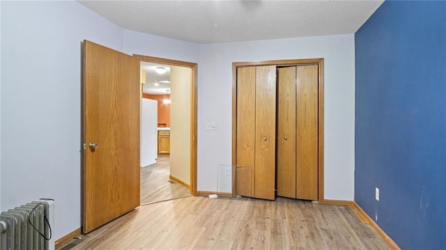 unfurnished bedroom featuring baseboards, radiator heating unit, a closet, and light wood-style floors