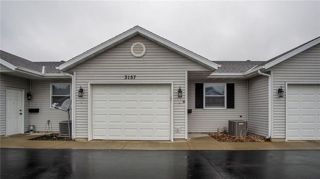 view of front of home featuring a garage, driveway, central AC, and roof with shingles