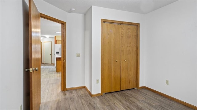 unfurnished bedroom featuring light wood-style floors, white fridge with ice dispenser, baseboards, and a closet