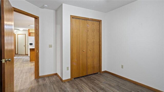 unfurnished bedroom featuring white refrigerator with ice dispenser, a closet, wood finished floors, and baseboards