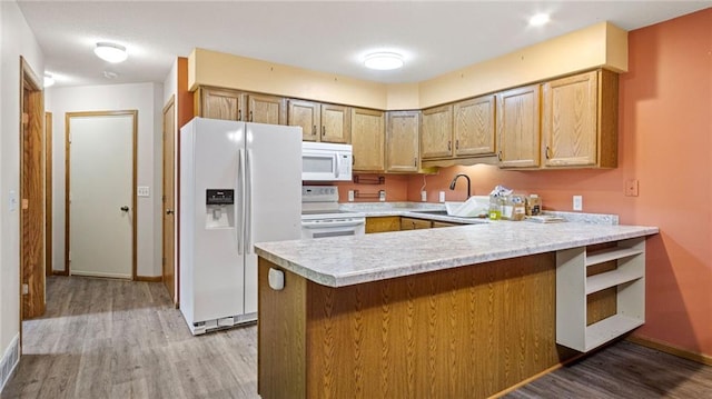 kitchen featuring a peninsula, white appliances, a sink, light countertops, and light wood finished floors