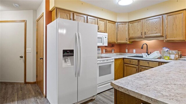 kitchen featuring white appliances, light wood finished floors, a sink, and light countertops