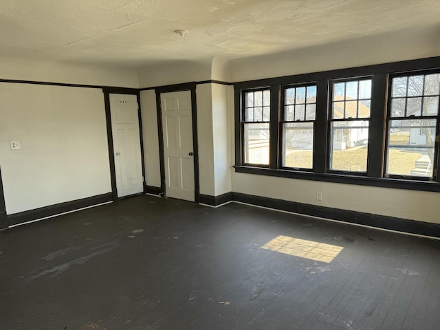 spare room featuring dark wood-style flooring, a textured ceiling, and baseboards